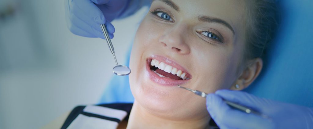 A man and woman smile as a dentist examines her teeth in a bright, welcoming dental office.